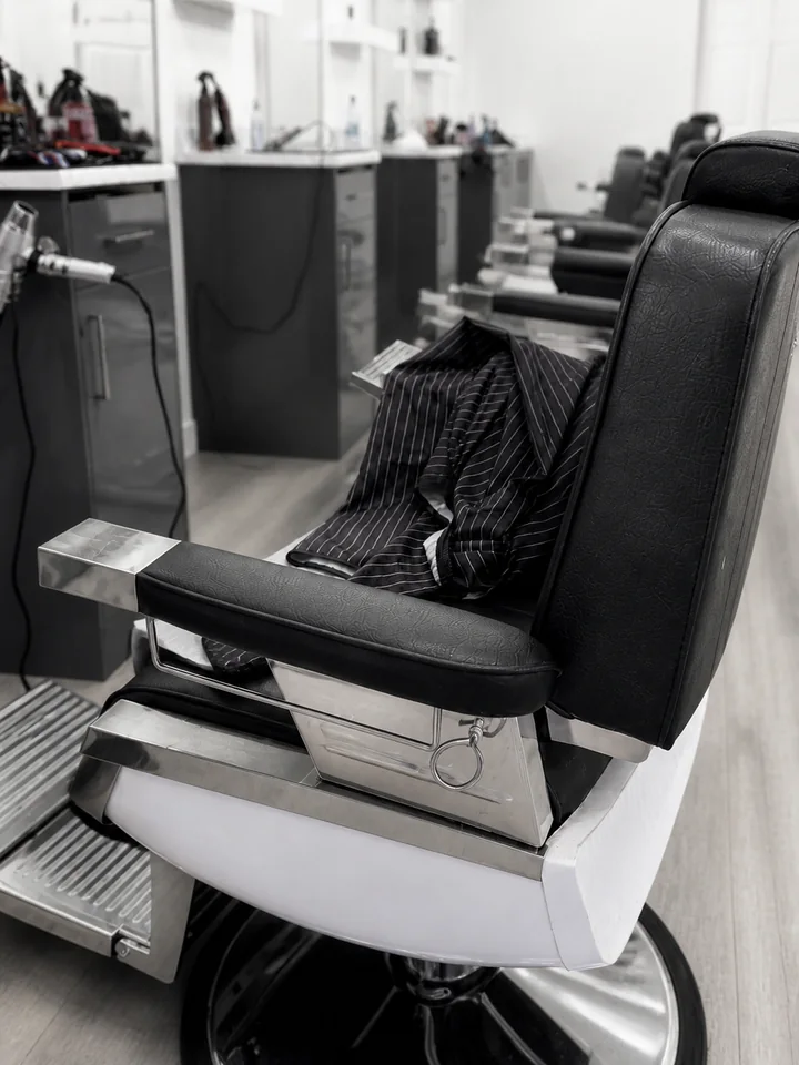 Black barber chair with polished chrome hardware and pinstriped cape at Bladez Affair